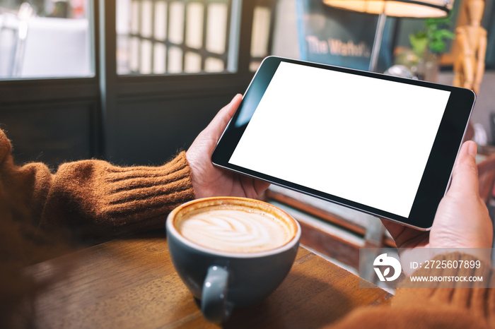 Mockup image of hands holding black tablet pc with blank white screen with coffee cup on wooden tabl