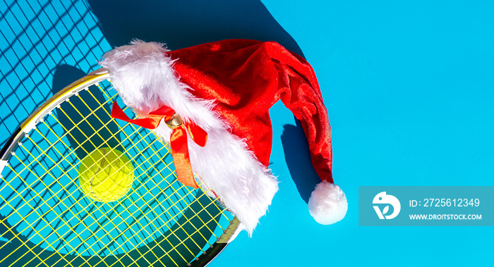 Santa Claus hat on tennis racket with ball on blue background.