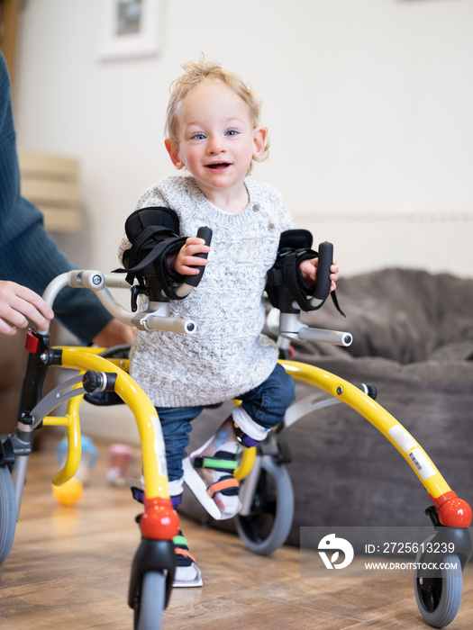 Boy with cerebral palsy using mobility walker with mother assisting�