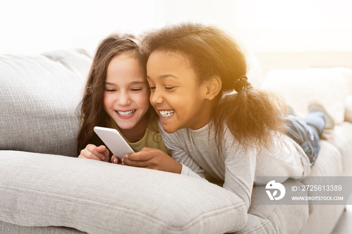 Best multiracial friends using smartphone, lying on sofa