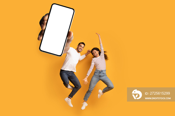 Wow, great news. Overjoyed couple showing huge smartphone with blank white screen, jumping and celeb