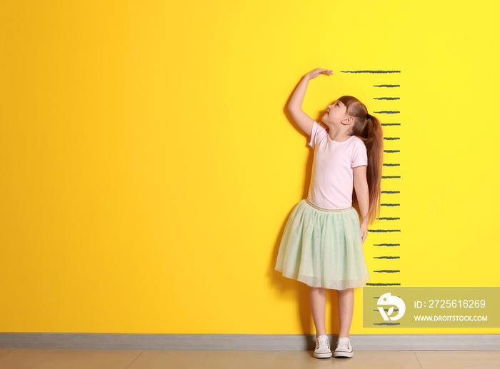 Cute little girl measuring height near color wall