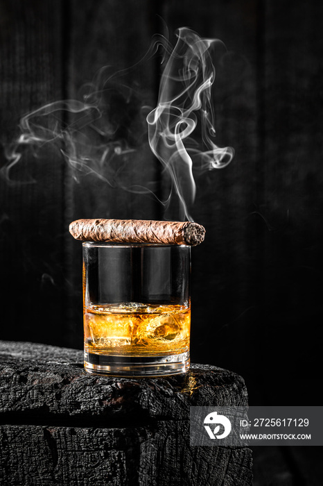 Smoking cigar on a glass of whiskey with ice