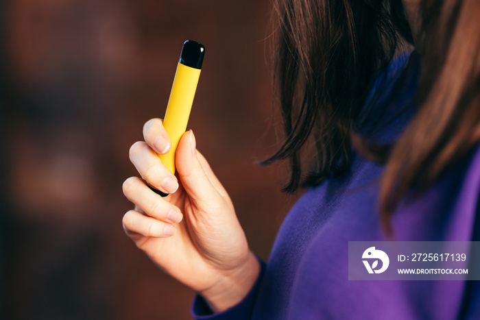 Yellow disposable electronic cigarette in a womans hand. Modern smoking