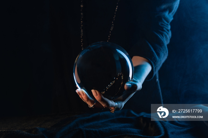 Partial view of crystal ball in female hand on dark blue