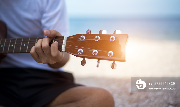 Close up handsome man playing classic guitar sitting on the beach in vacations.