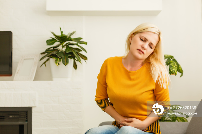 girl having period is sitting on sofa and feeling much of painful on her stomach and twist her body.