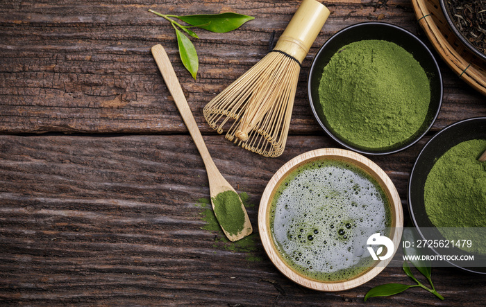 Japanese organic matcha green tea powder in bowl with wire whisk and green tea leaf on wooden backgr