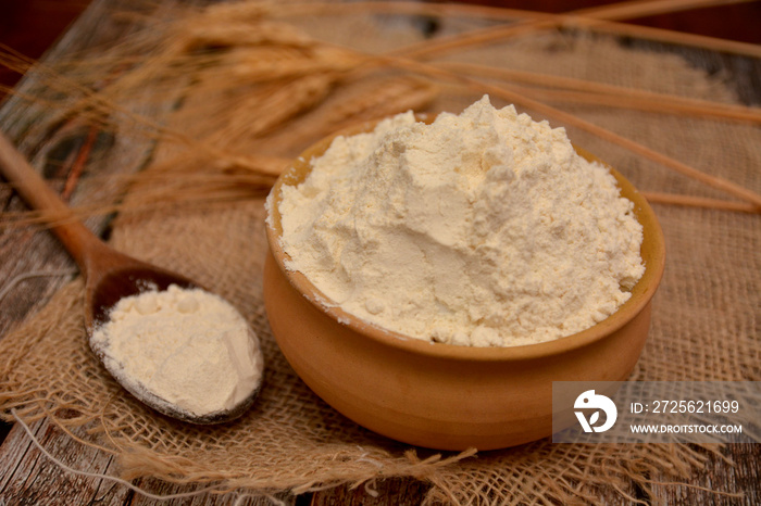 farina bianca in contenitore di terracotta con spighe di grano sul fondo