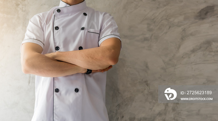 Handsome caucasian man professional Chef arms crossed in white uniform on gray cement wall with copy