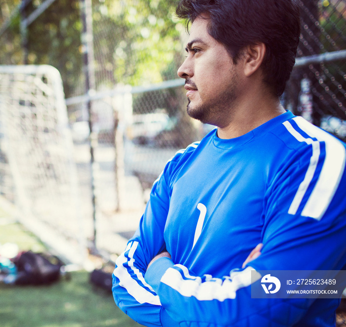 Man with arms crossed looking away while standing at soccer field