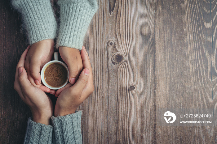 Two people holding cup of coffee in hands with love and warmth on wooden table