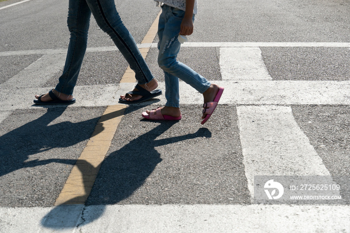 Mother and childs legs walk across the zebra crossing on an asphalt road.