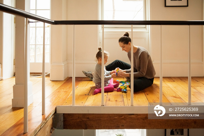 Side view of mother with daughter arranging colorful alphabets on hardwood floor at home