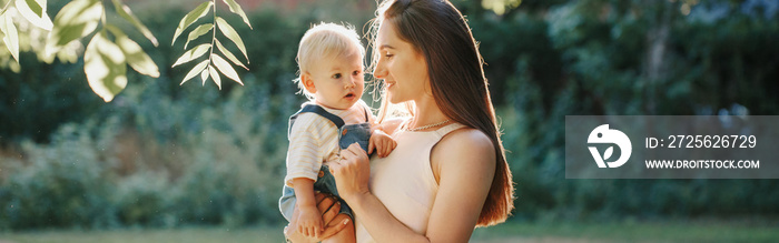 Mothers Day. Young smiling Caucasian mother and boy toddler son hugging in park. Mom holding carryin