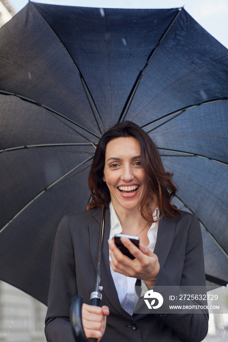 Portrait smiling businesswoman with umbrella using smart phone