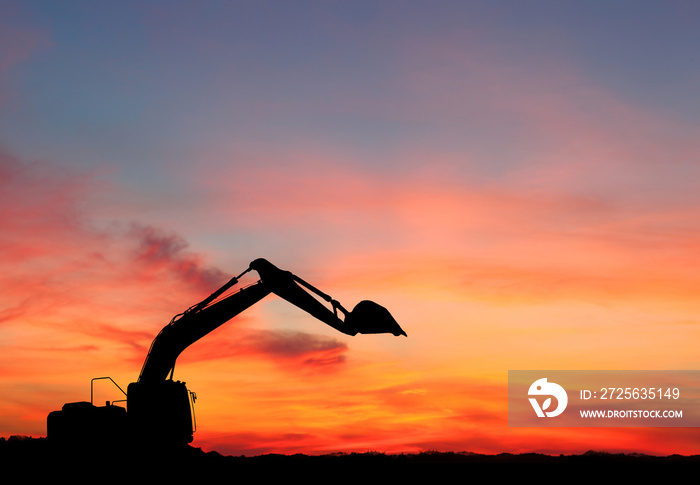 silhouette of Excavator loader at construction site with raised bucket over sunset