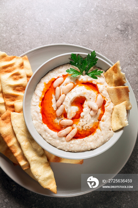 Hummus of white beans with spicy oil of hot pepper and homemade crispy loaves on a gray stone table