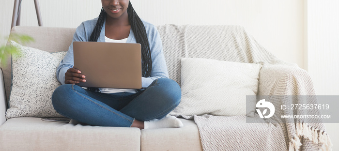 无法辨认的非洲女孩坐在家里的沙发上使用笔记本电脑