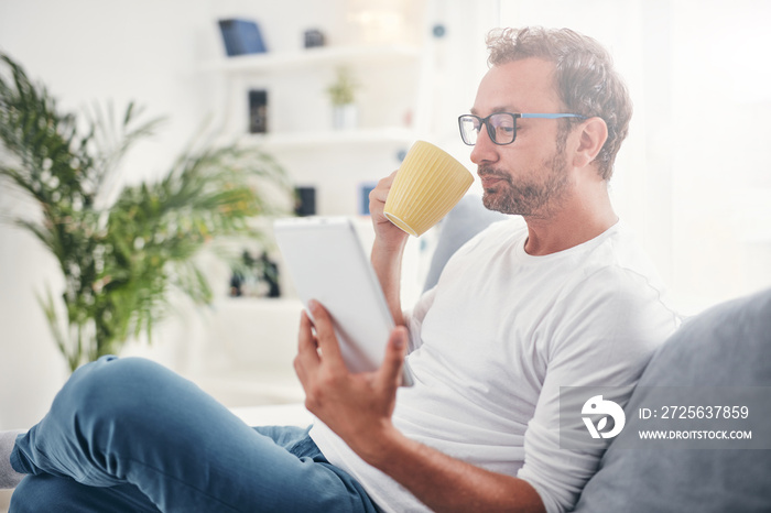 Man holding tablet, surfing online and drinking coffee.