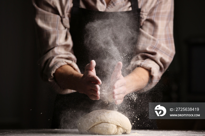 Male hands clapping and sprinkling flour over dough on black background