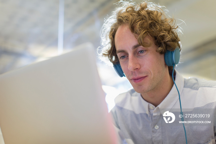 Businessman with headphones working at laptop in office