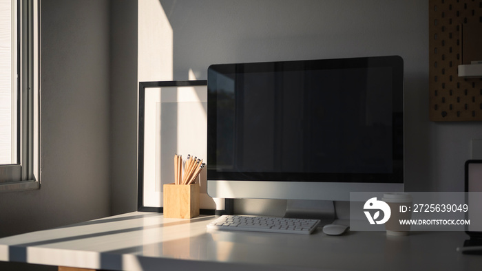 Modern home office with computer and office supplies on white table near window.