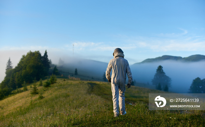 宇航员太空旅行者穿着太空服在绿草上行走，前往雾山的背面视图