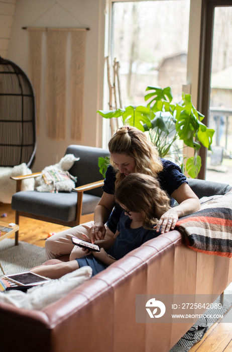 High angle view of mother with daughter using smart phone while sitting on sofa against windows at h