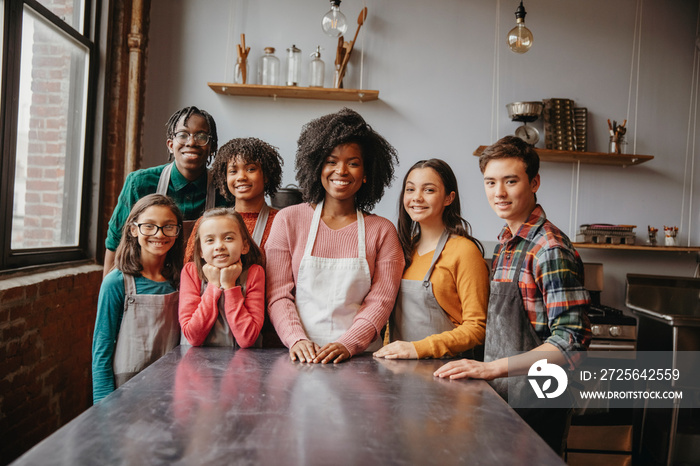 Portrait of smiling female chef with students standing by table against wall in cooking class