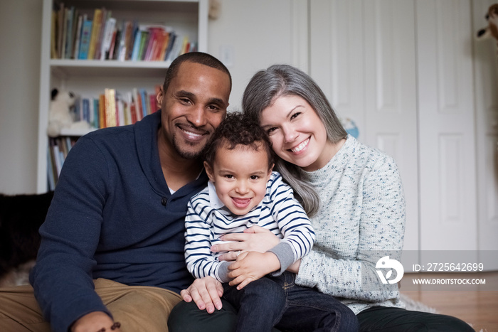 Portrait of happy parents with cute son sitting against wall at home