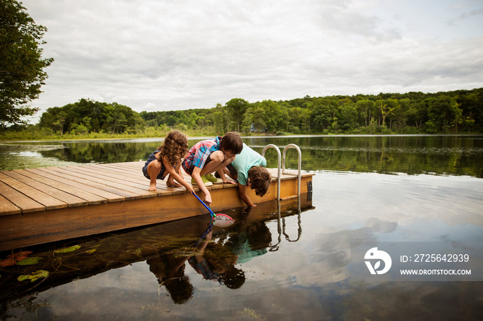 Children crouching on jetty and playing in water