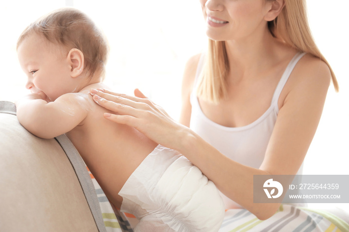 Woman applying body cream on her baby indoors