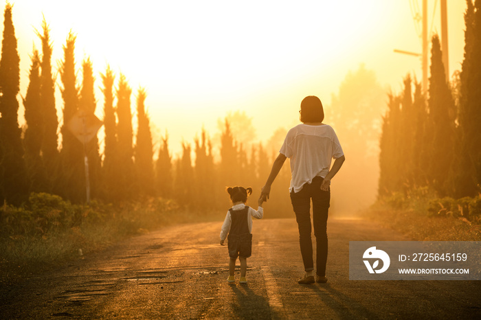 Mother and child holding hands at sunset with copy space, view from the back