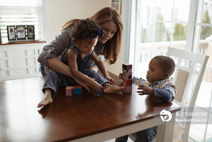 Mother with children arranging toy blocks on wooden table at home