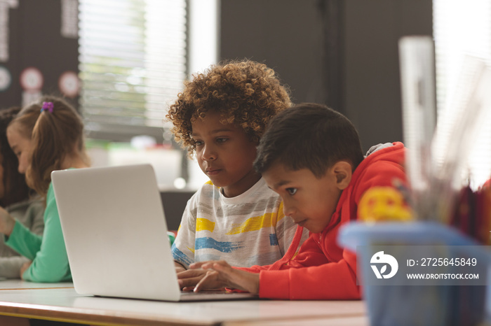 Front view of two school kids working on one laptop in classroom