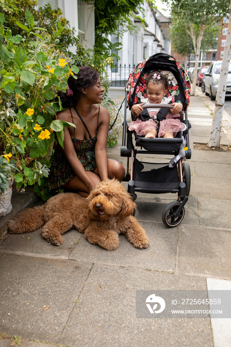 母亲带着婴儿车和狗带着12-17个月大的女儿散步