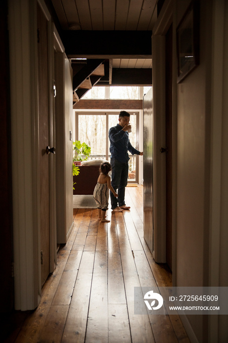 Side view of father drinking water while standing with daughter on hardwood floor at home