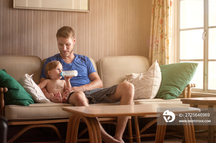 Baby boy with his father drinking milk on sofa