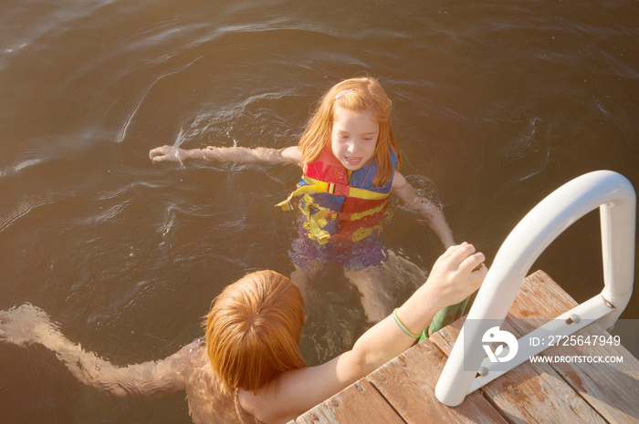 Kids (6-7, 12-13) swimming in lake near pier