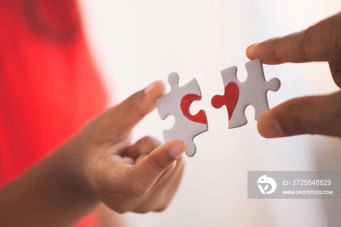 Parent and kid hands connecting couple jigsaw puzzle piece with drawn red heart