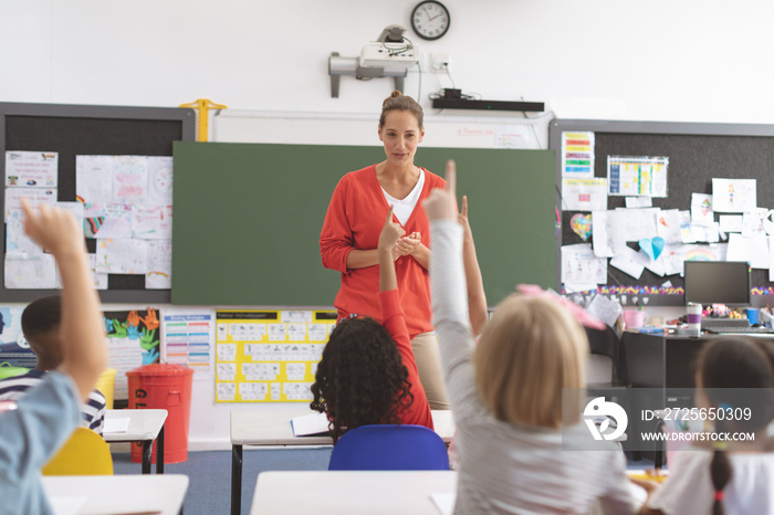 Rear view of school kids raising hand to answer at a question