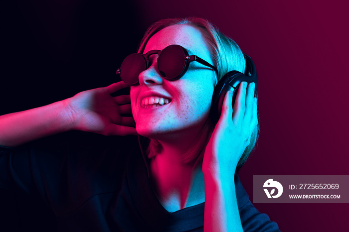 Happy pretty woman with headphones listening to music over red neon background at studio.