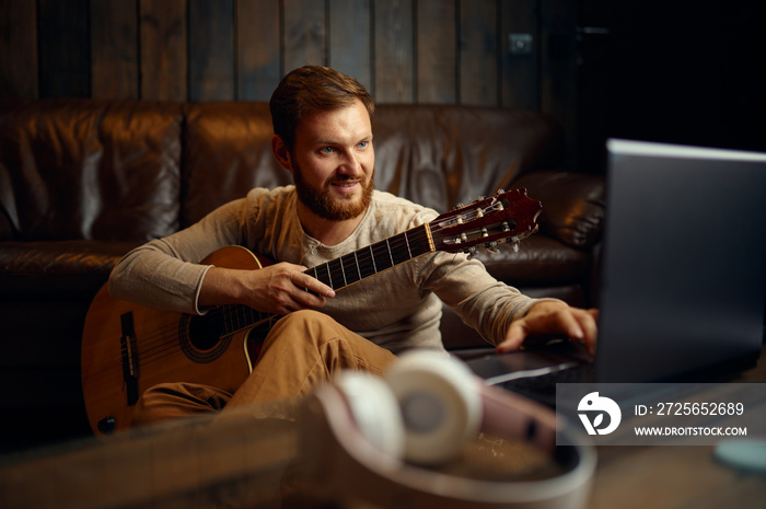 Man playing guitar listening looking at laptop