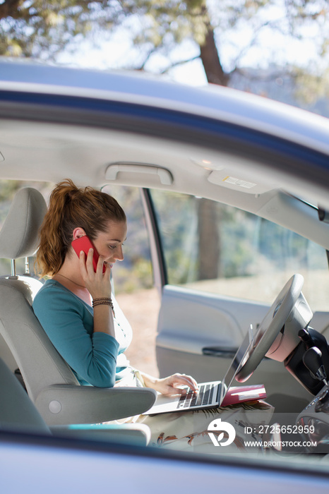 Woman with laptop and smart phone working inside car