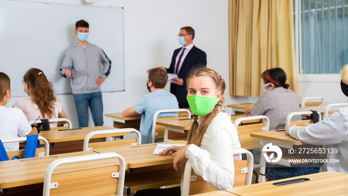 Portrait of teenage schoolgirl in protective face mask during lesson in college. Concept of necessar