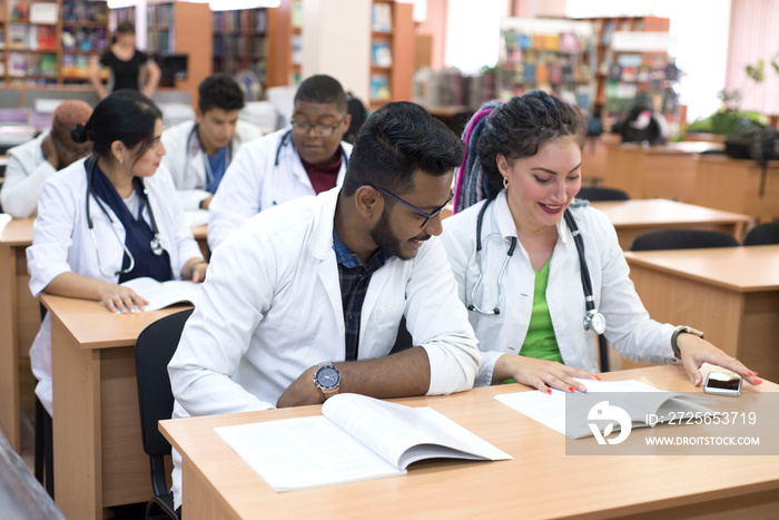 一群年轻的跨国医学生坐在桌子旁，学习课本，面带微笑