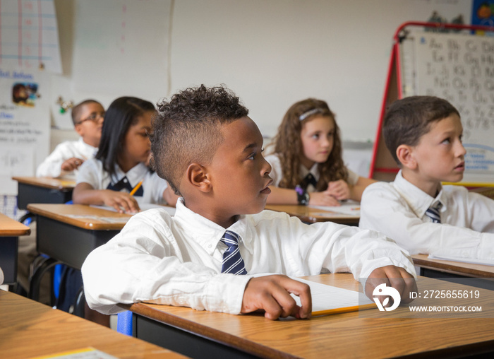 Portrait of schoolboy (8-9) sitting at desk in classroom with other classmates in background