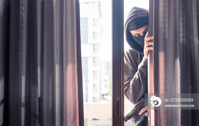 Burglar wearing black clothes and leather coat breaking in a house