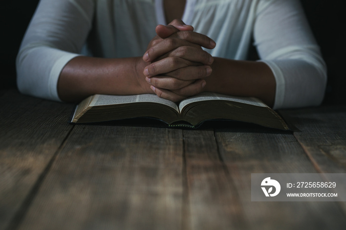 Hands folded in prayer on a Holy Bible in church concept for faith